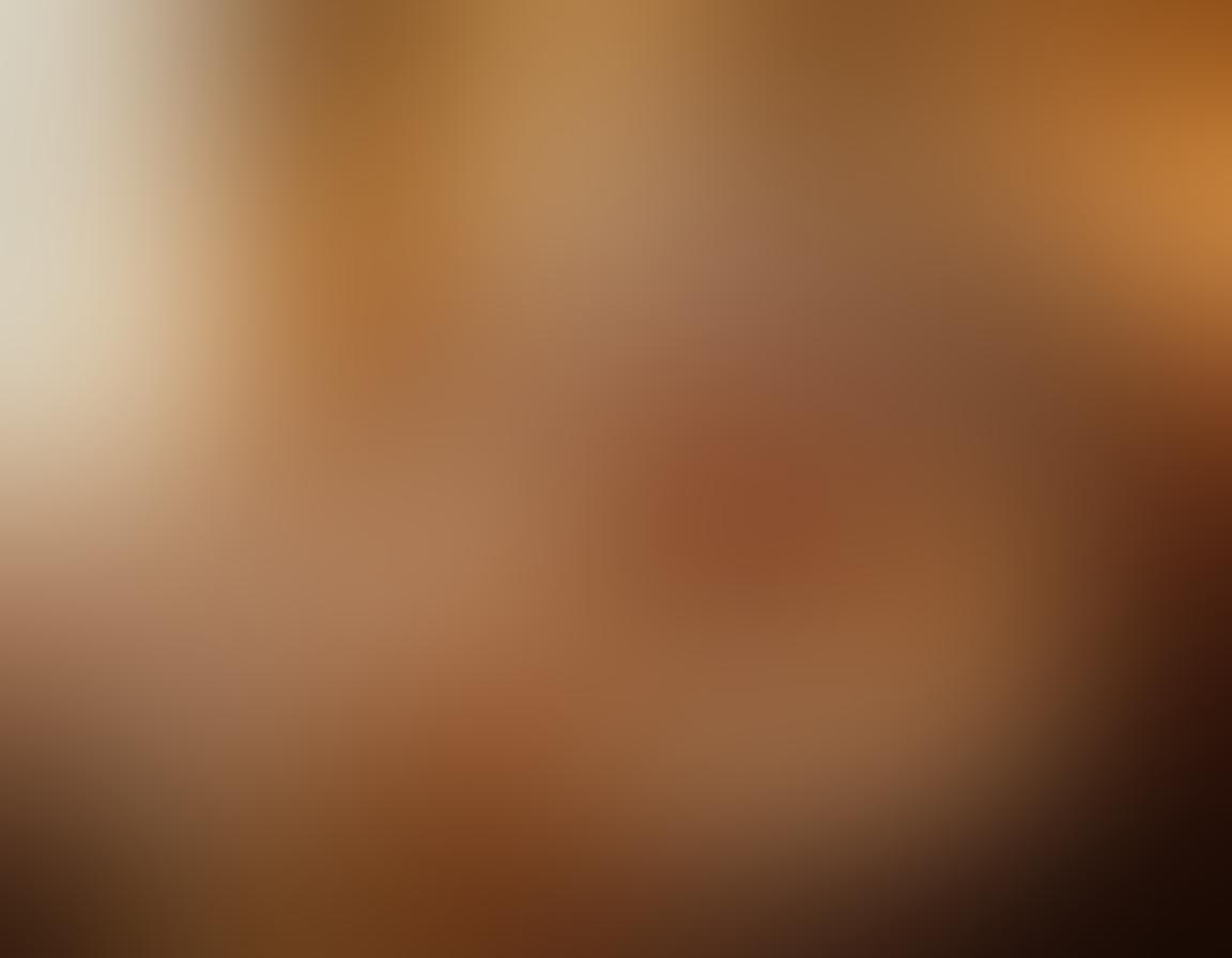 A warm and inviting scene featuring an elegantly aged couple enjoying a playful moment in a cozy, dimly-lit room adorned with tasteful art that embodies nude figures. The couple is laughing, surrounded by soft pillows and rich fabrics, creating an intimate atmosphere. Accentuate soft golden lighting to symbolize warmth and connection. Ethereal touches, like floating petals, add a sense of romance. vibrant colors. super-realistic.